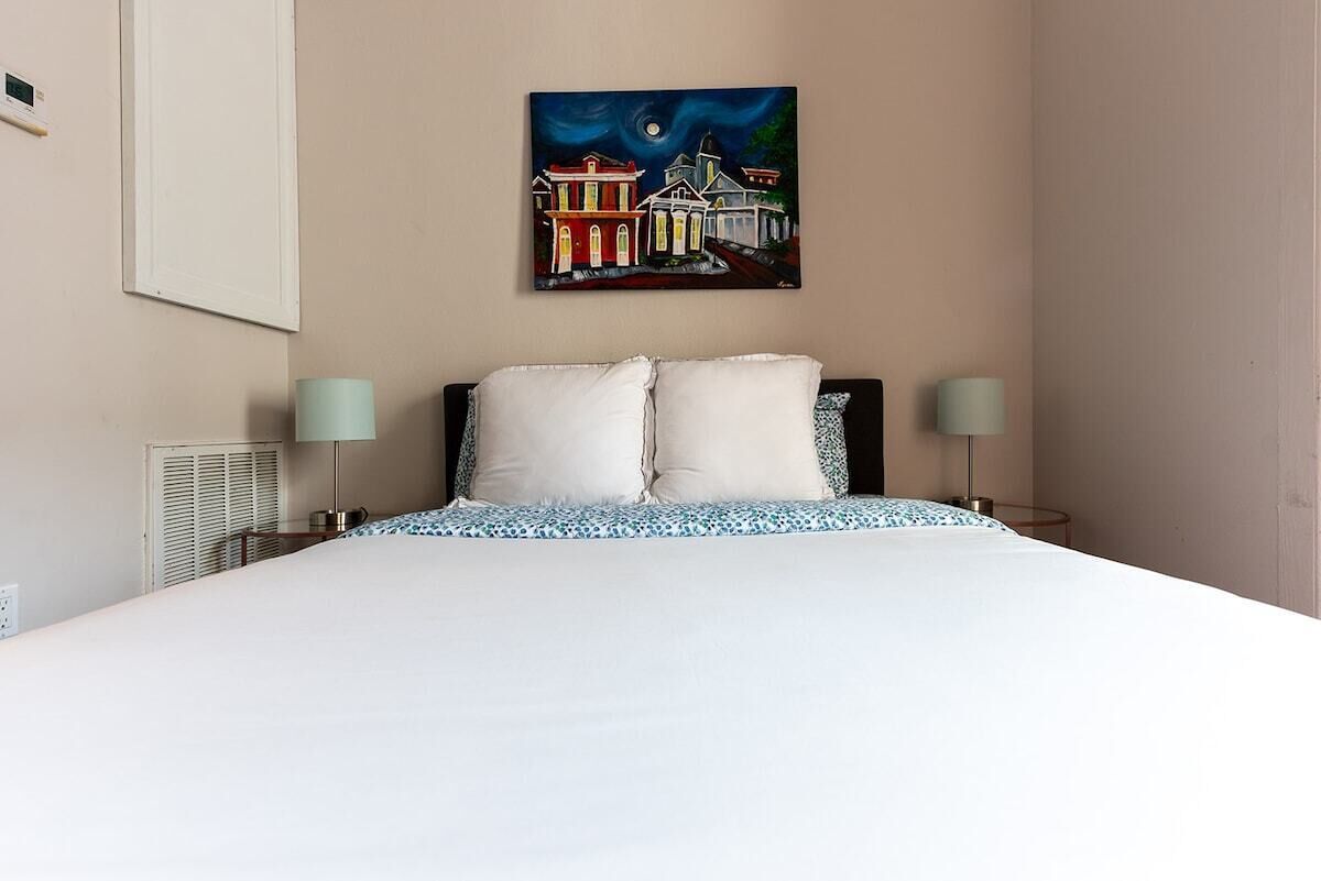 Habitación de hotel con una cama grande, dos lámparas de noche, un cuadro en la pared y una ventana con persianas.
