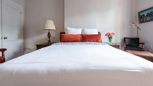 A neatly made bed with white and orange bedding, a bedside lamp, and a vase with pink flowers. - Enchanting Garden District Magazine Street Flat (New Orleans)