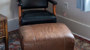 A room with a black leather chair, a brown leather ottoman, a floor lamp, and a painting on the wall. - Enchanting Garden District Magazine Street Flat (New Orleans)
