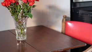 A table with a vase of red flowers, a wooden chair with a red cushion, and a kitchen area with a microwave and oven. - Enchanting Garden District Magazine Street Flat (New Orleans)
