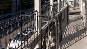 Un balcón cubierto con barandilla de metal, con vistas a una calle con coches y edificios.