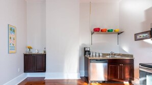 Una cocina con armarios de madera oscura, lavavajillas, cafetera y una estantería con cuencos de colores.