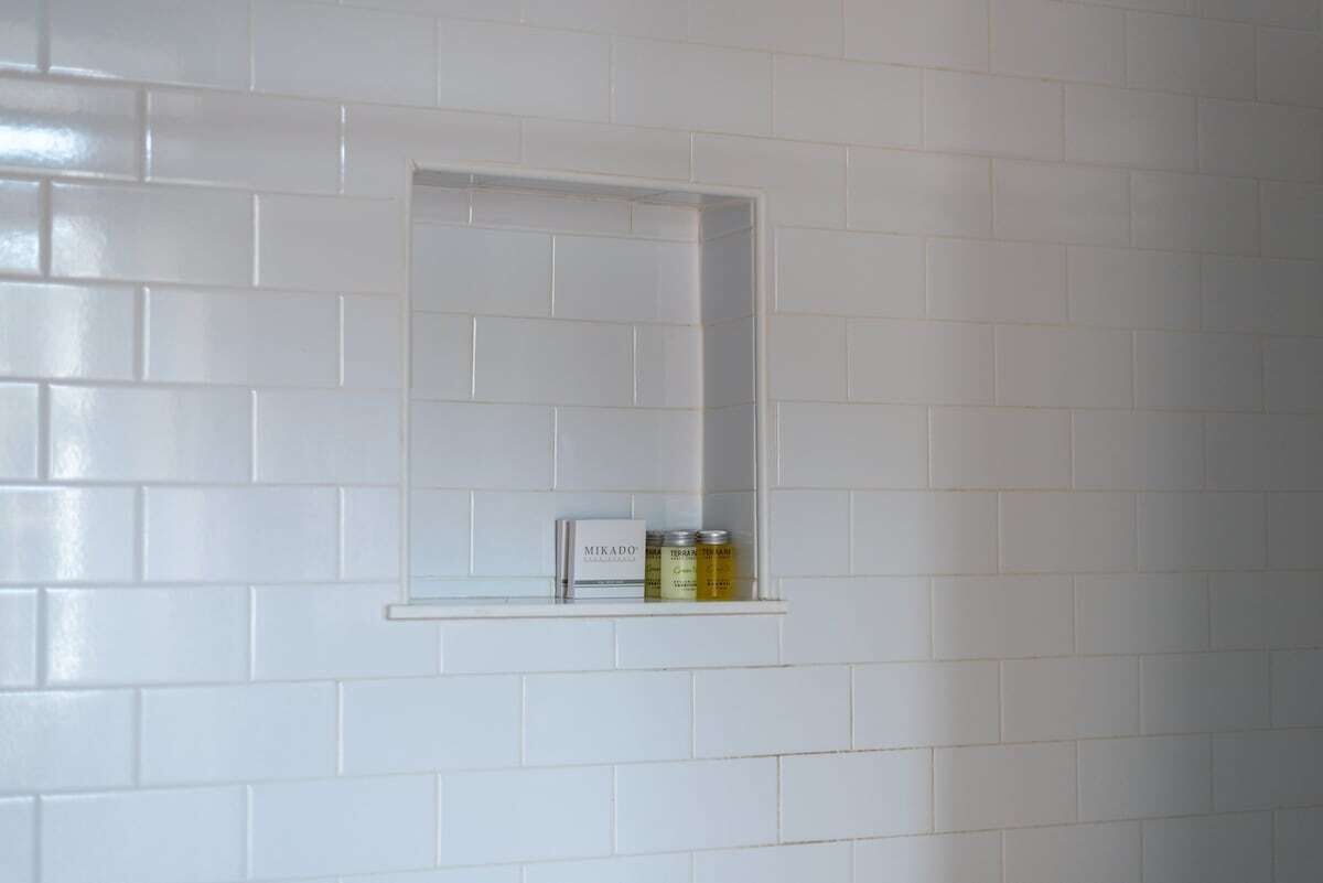 A bathroom with white subway tiles and a small shelf with a bottle and a container.
