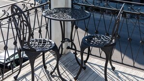 Un balcón con cuatro sillas de metal y una pequeña mesa redonda, con vista a un edificio moderno con grandes ventanales.
