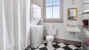 Een badkamer met een wit toilet, een wastafel, een raam en een douchegordijn.