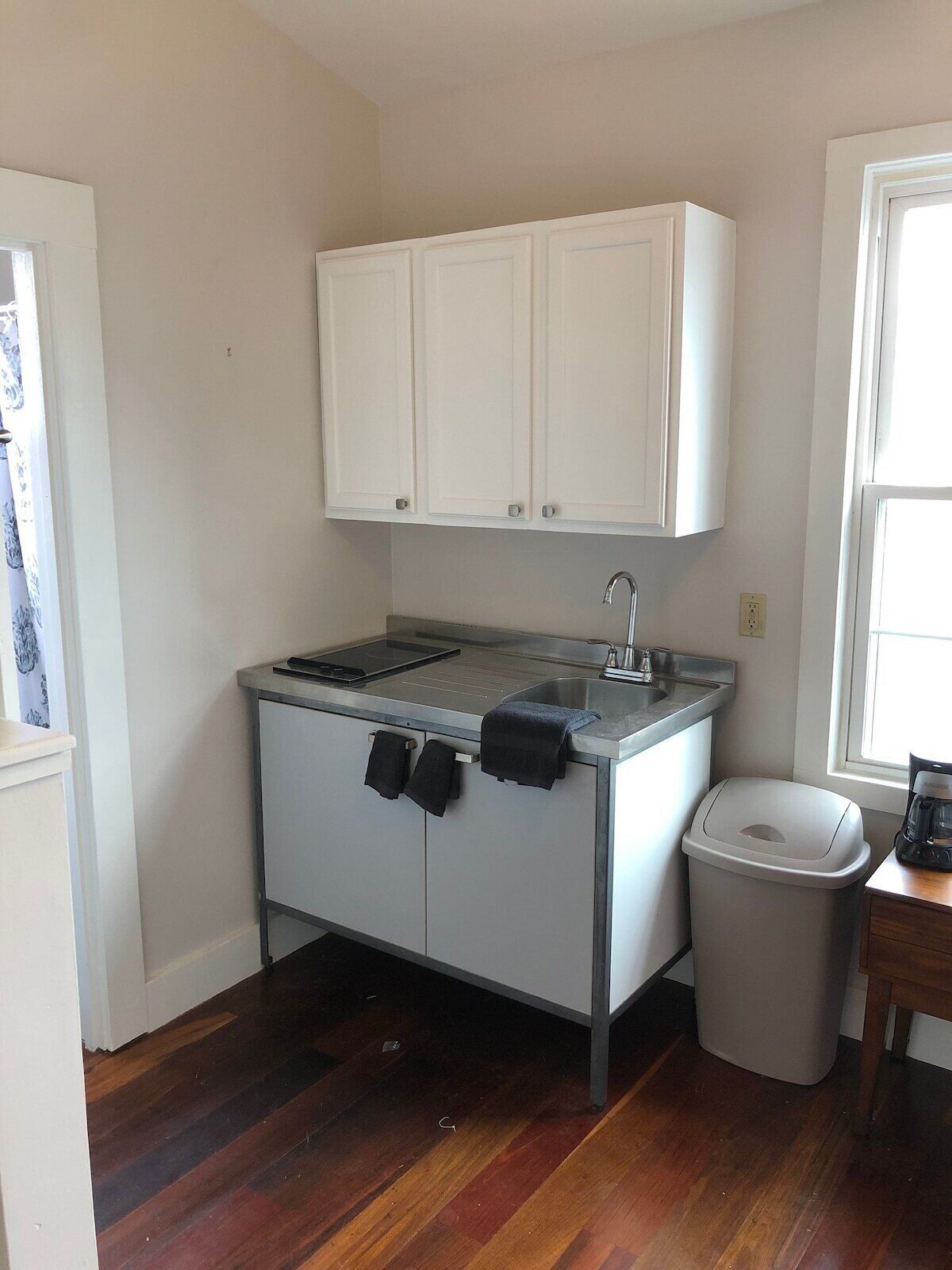 A compact kitchen with white cabinets, a stainless steel sink, and a trash bin.