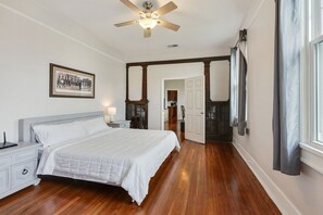 Une chambre à coucher avec un lit, une table de chevet, un ventilateur de plafond et un tableau encadré au mur.