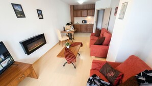 A modern living room with a fireplace, a red sofa, a dining area, and a kitchen in the background.