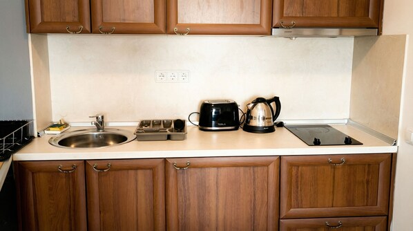 A kitchen with wooden cabinets, a stainless steel sink, a toaster, a kettle, and a black induction cooktop.