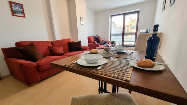 A modern living room with a red sofa, a dining table set with plates, bowls, and a bottle.
