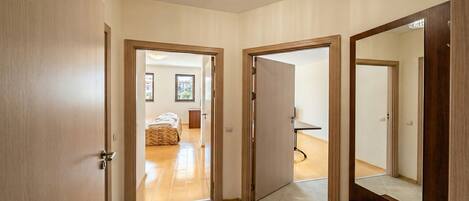 A hallway with wooden doors leading to a bedroom with a bed and a view of the outside.
