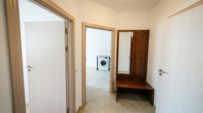 A hallway with a wooden bench, a washing machine, and a mirror on the wall.
