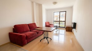 A modern living room with a red sofa, a wooden coffee table, and a balcony with a city view.