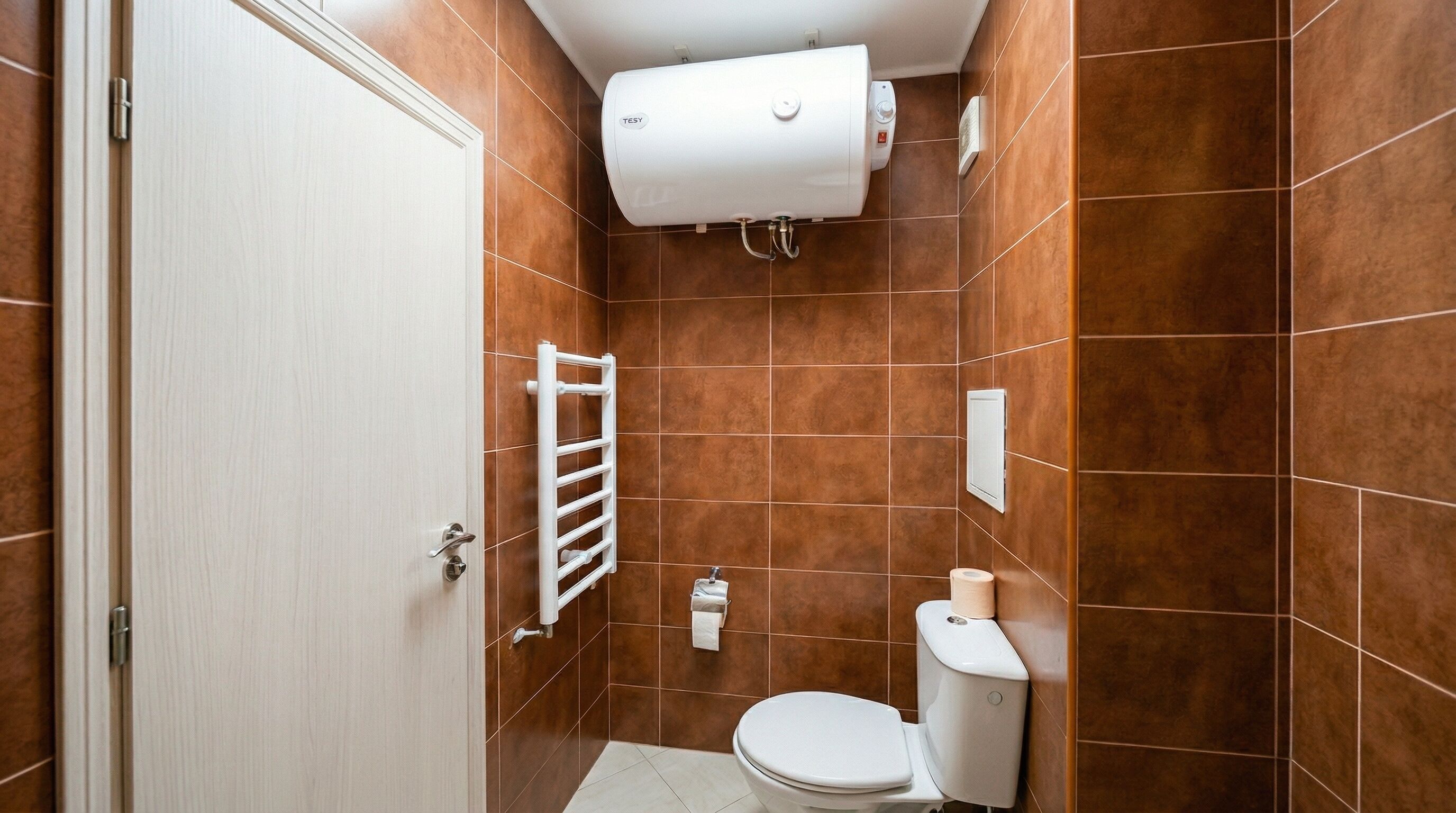 Un bagno piccolo rivestito di piastrelle marroni, con un WC bianco, un portasciuga e un termosifone a parete.