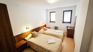 A small, clean room with two beds, a wooden nightstand, a desk, and a radiator. - Mountain Paradise 4 - 1 Bedroom - Gondola, 100m Away - Washer (Bansko)