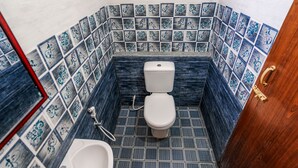 Un baño con inodoro, bidé y lavamanos, con azulejos blancos y azules con diseño.