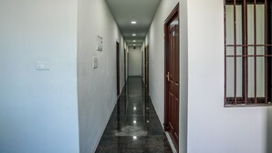 Un pasillo con piso pulido, paredes blancas y una ventana con rejas.