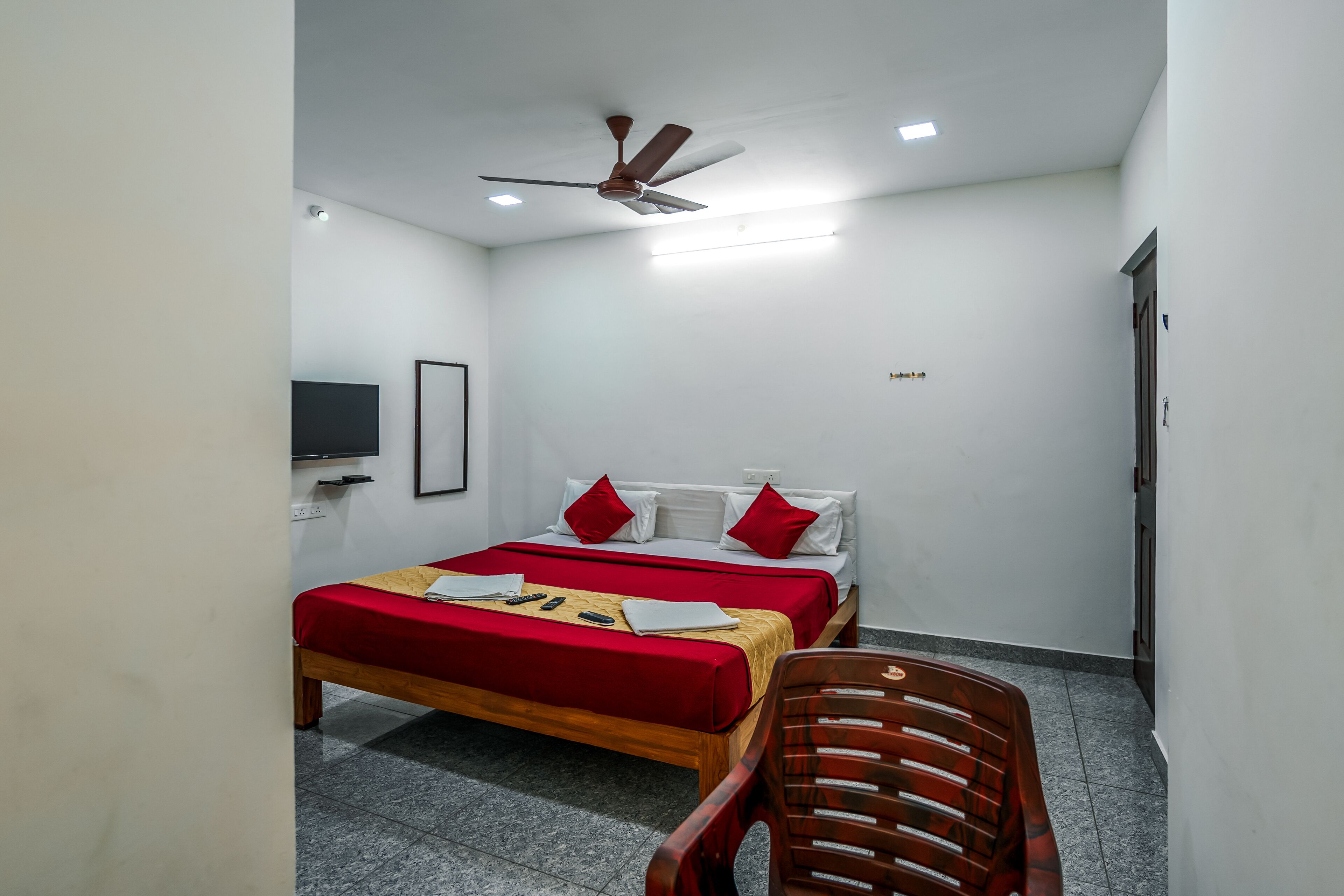 Une chambre à coucher avec un lit, un ventilateur de plafond, une télévision et une chaise.