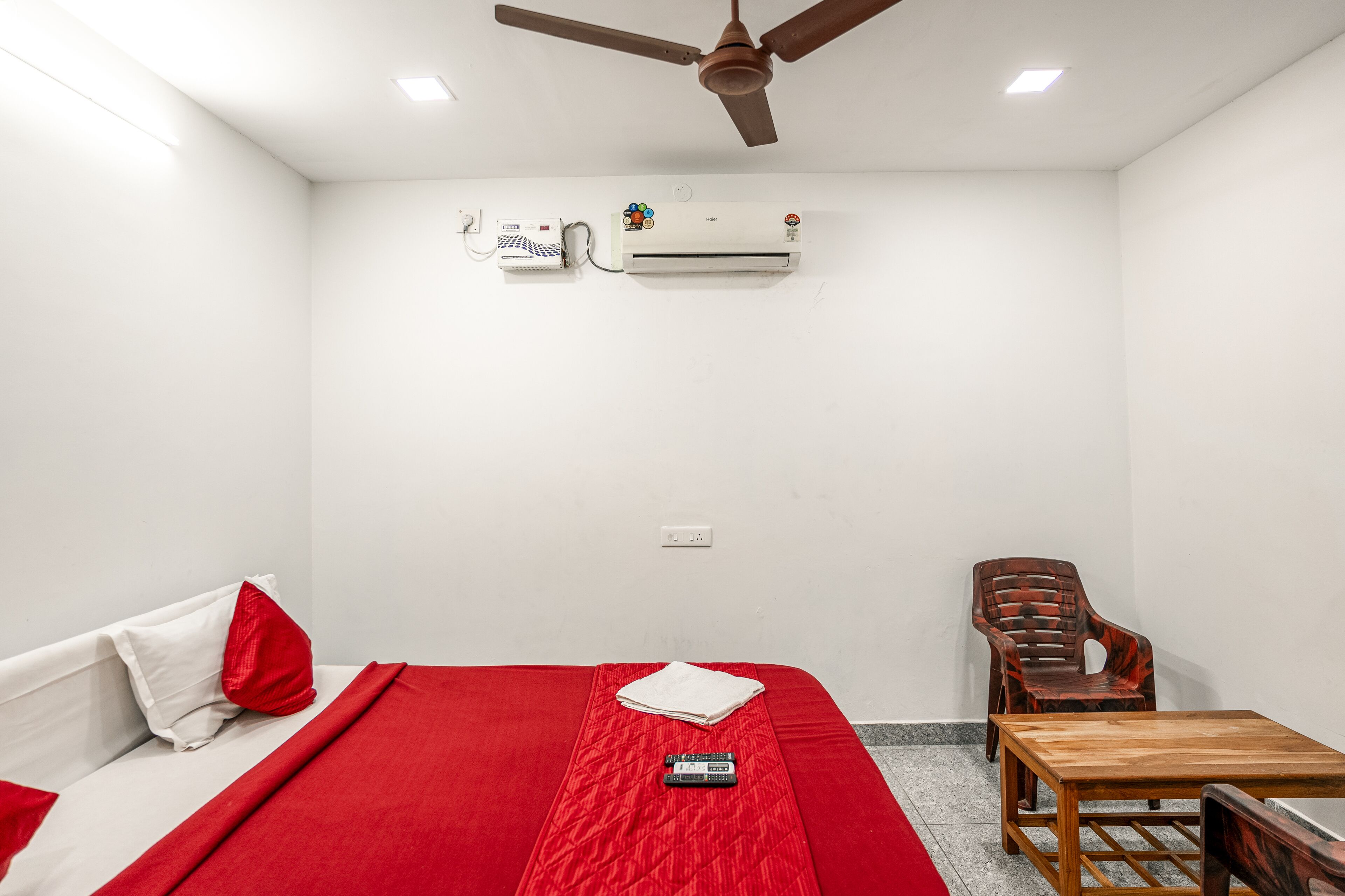 Une pièce comprenant un lit, une table, une chaise, un climatiseur et un ventilateur de plafond.