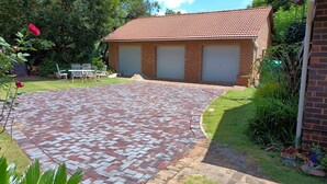 A brick building with a tiled roof, a paved driveway, and a small garden area with plants and a table.