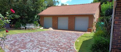 A brick building with a tiled roof, a paved driveway, and a small garden area with plants and a table.