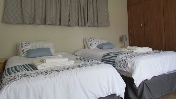 A hotel room with two beds, each with a white comforter and blue accents, a grey curtain, and a wooden wardrobe.