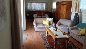 A living room with a sofa, armchair, and a wooden coffee table. There is a ceiling fan and a window with curtains.