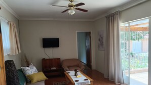A living room with a ceiling fan, a flat-screen TV, a wooden cabinet, a sofa, a chair, and a table with a placemat.