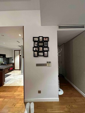 A modern interior with a wall-mounted photo collage, a white door with a handle, and a hallway leading to a kitchen area.