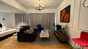 Un salon moderne avec un canapé noir, un fauteuil rouge, un téléviseur et un lustre.