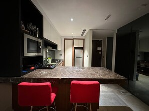 A modern kitchen with a marble countertop, two red bar stools, and a built-in microwave.