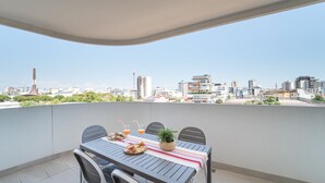 A balcony with a table set for two, featuring a striped tablecloth, a potted plant, and a plate of food.