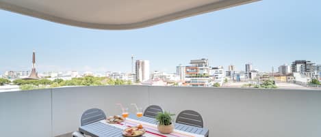 Un balcon avec une table dressée pour deux personnes, agrémentée d’une nappe à rayures, d’une plante en pot et d’une assiette de nourriture.