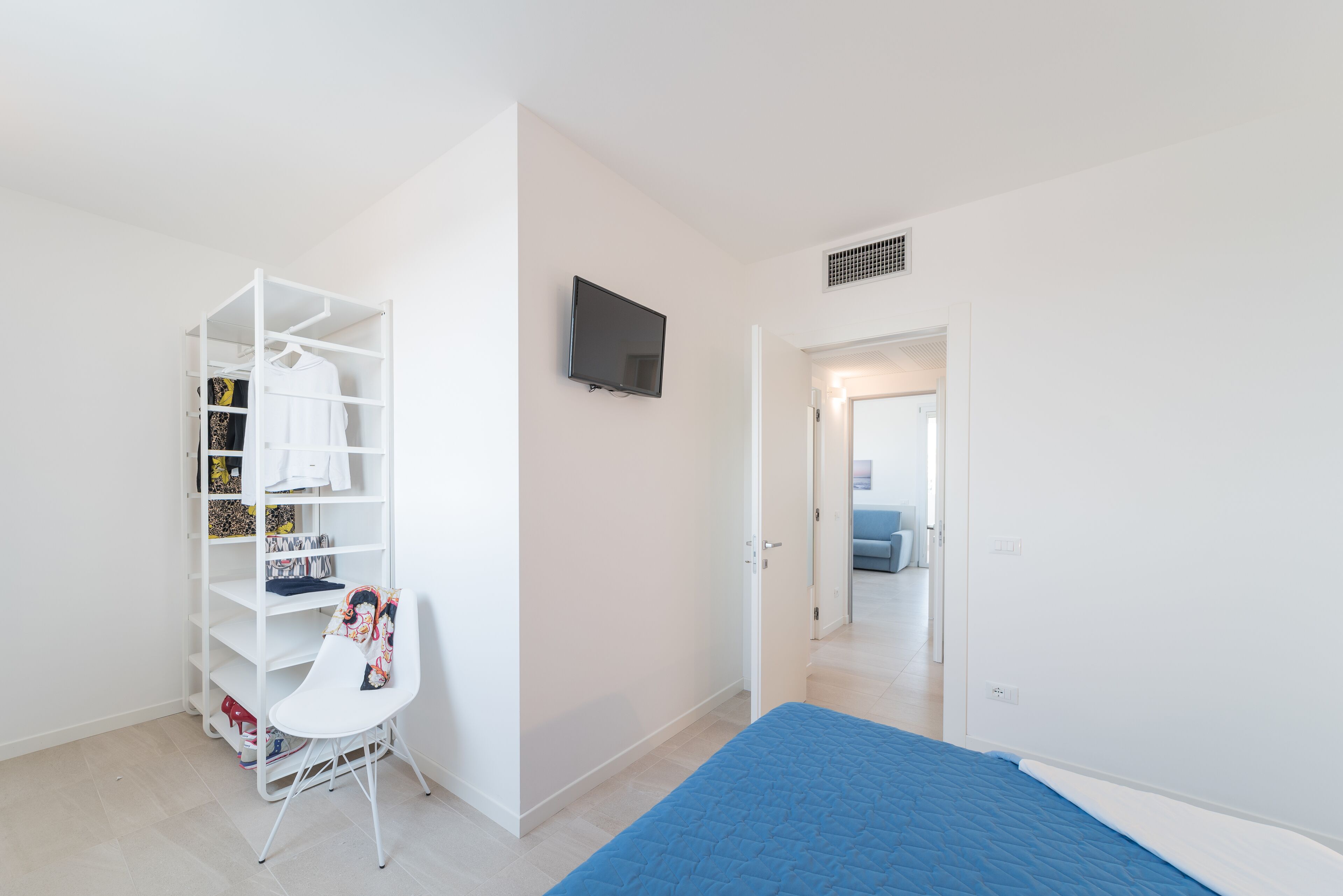 A bedroom with a bed, a white wardrobe, a chair, and a television.