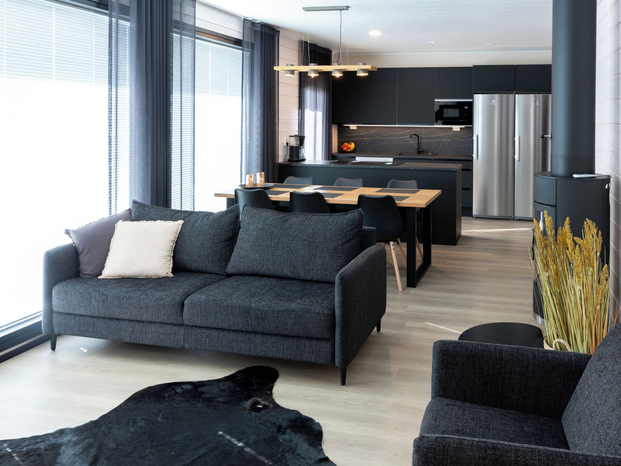 Een moderne woonkamer met een bank, een salontafel en een hond. In de achtergrond is een keuken te zien met een koelkast en een magnetron.