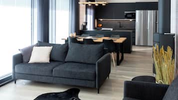 Een moderne woonkamer met een bank, een salontafel en een hond. In de achtergrond is een keuken te zien met een koelkast en een magnetron.