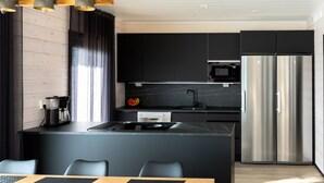 Une cuisine moderne dotée d’un îlot central, de meubles de couleur noire, d’appareils électroménagers en acier inoxydable et d’un coin repas avec une table en bois et des sets de table noirs.