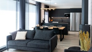 Un salon moderne avec un canapé gris, un chien noir et un coin repas comprenant une table et des chaises en bois.