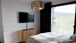Une chambre moderne avec un grand lit, un téléviseur fixé au mur et une fenêtre équipée de stores.