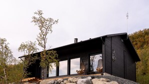 Une maison moderne dotée de grandes fenêtres, de fondations en pierre et d’une cheminée imposante.