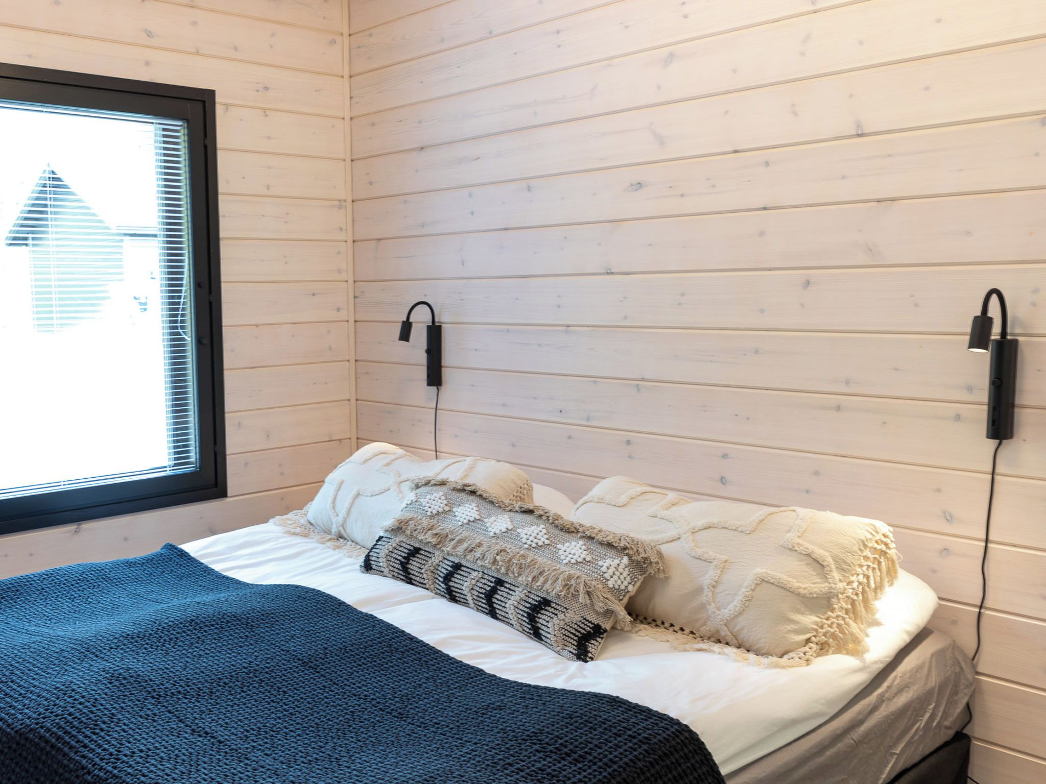 Een slaapkamer met een bed, een raam en een wandlamp.