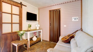 A room with a wooden sliding door, a white sofa, a small wooden table with a vase, a mounted TV, and a guitar leaning against the wall. - Vacation Home 'Los Diablitos 5' with Mountain View, Shared Terrace and Wi-Fi (Santa Cruz de Tenerife)