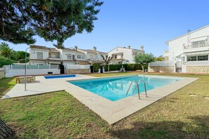 A swimming pool with a metal ladder, surrounded by a grassy area and a white fence.