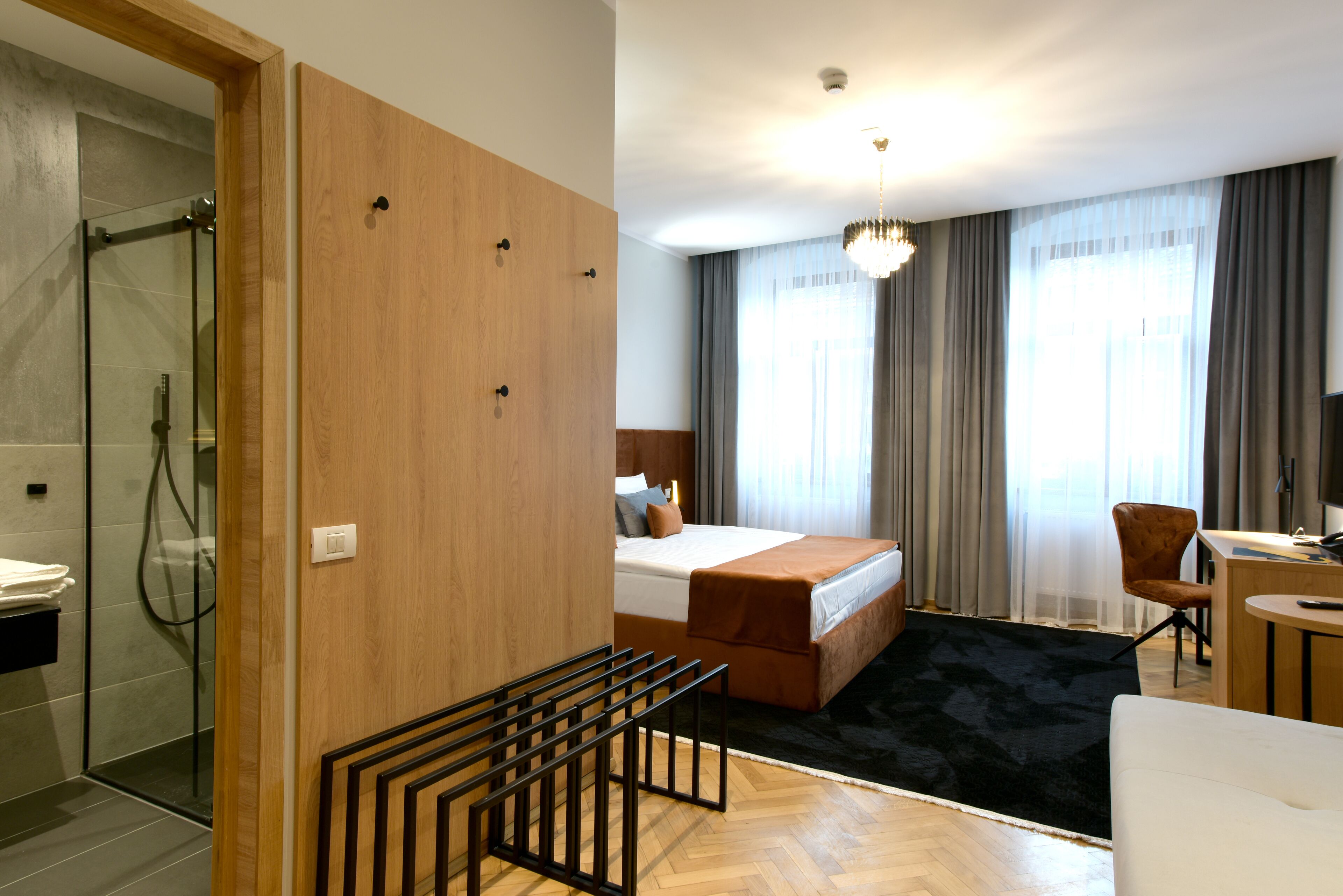 A hotel room with a shower, a bed with a headboard, a desk, and a chair.