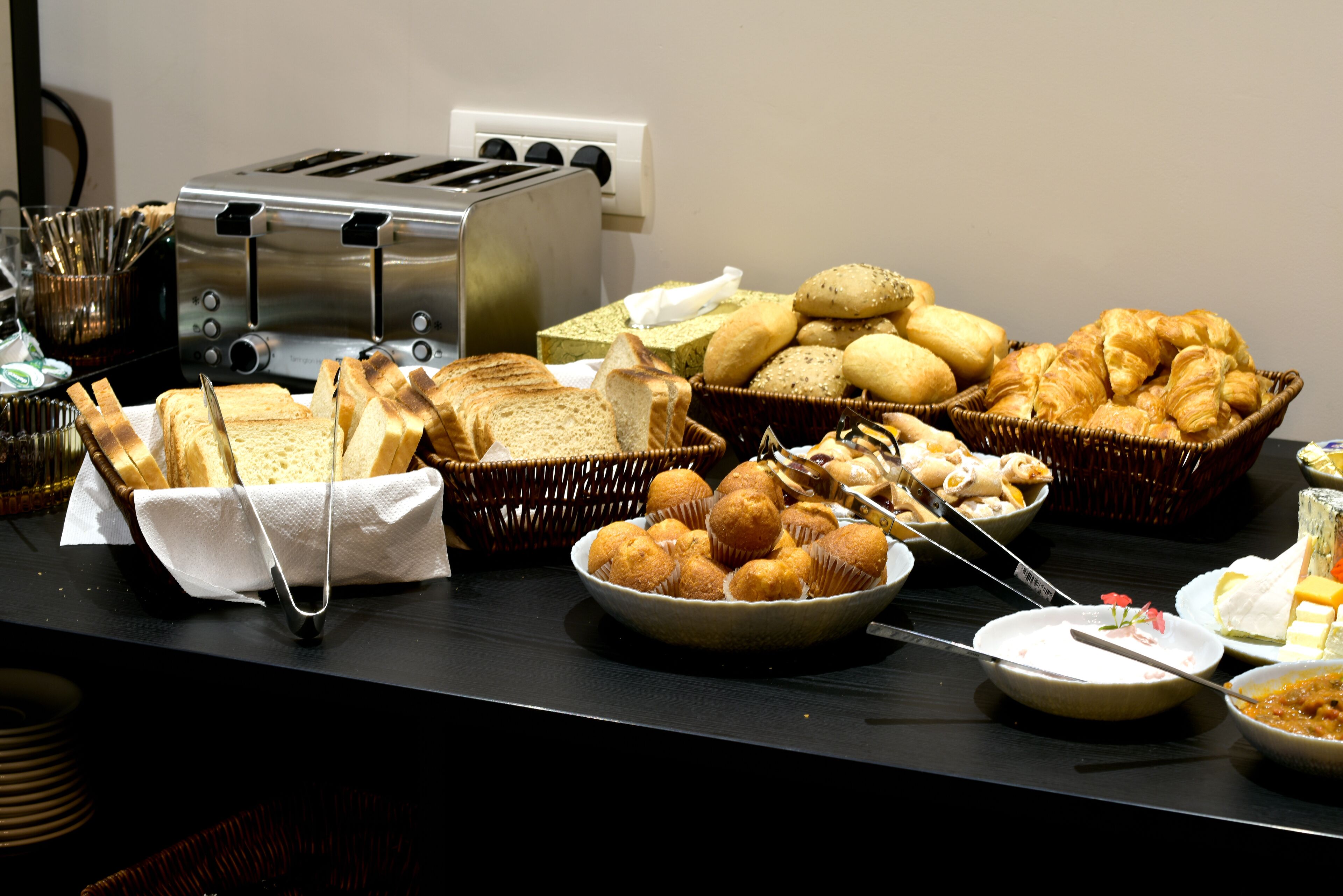 A buffet table with various breads, pastries, and a toaster.