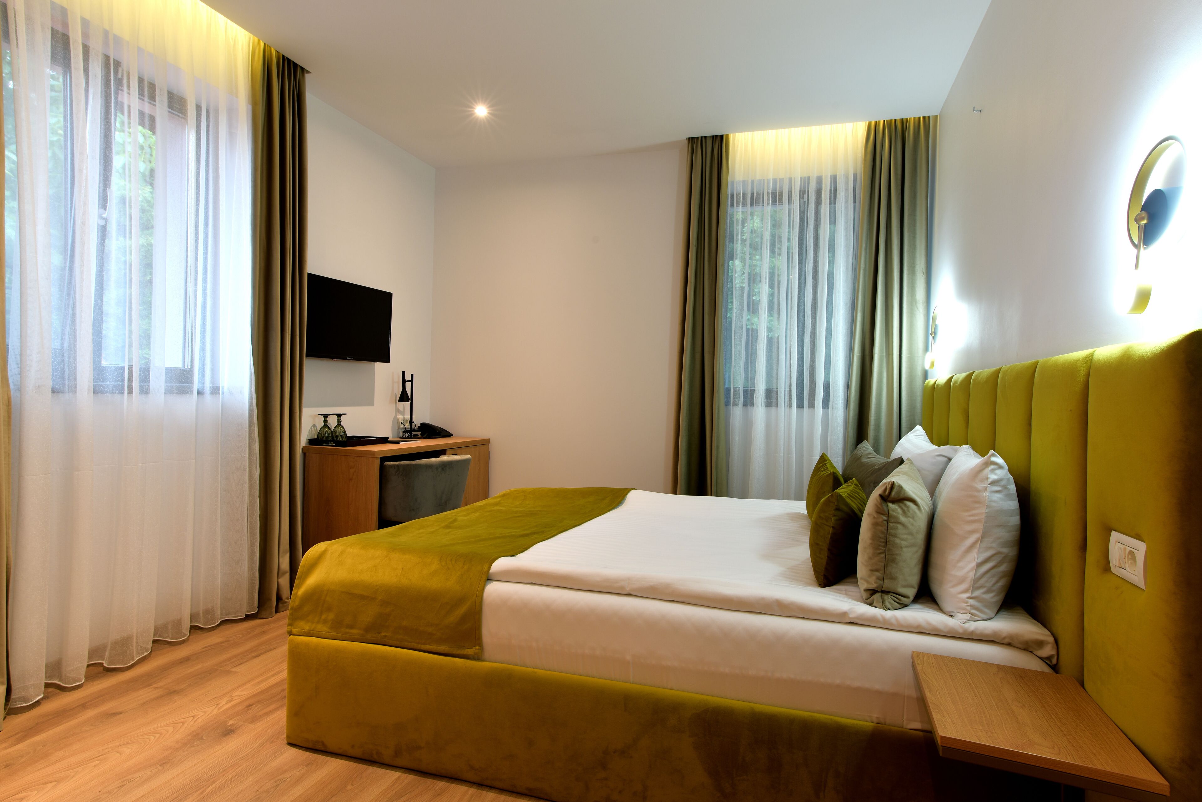 Una habitación de hotel con una cama, una mesita de noche y un televisor montado en la pared.