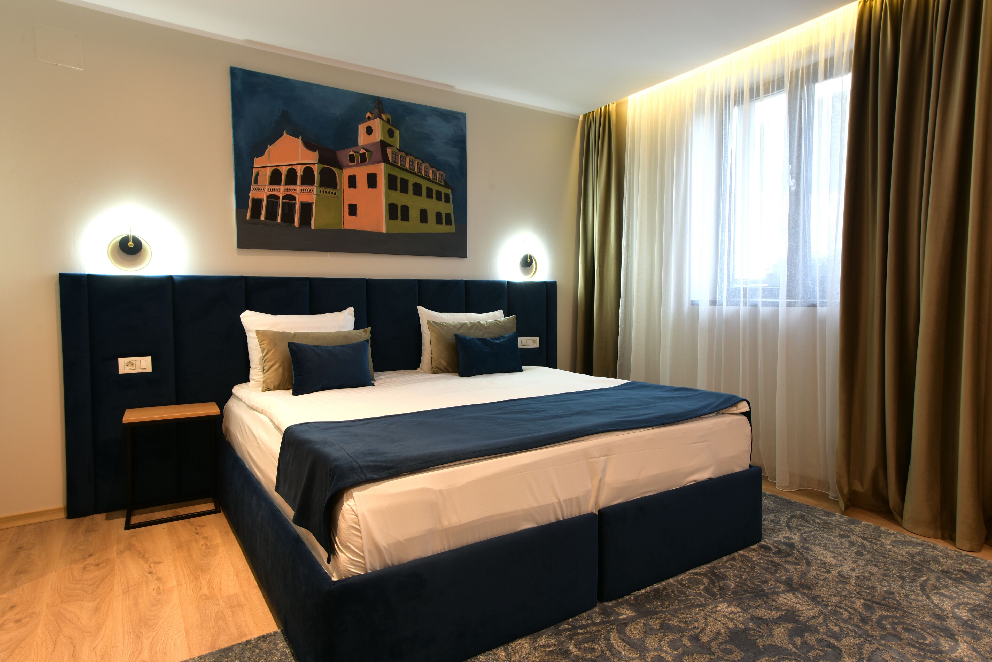Una habitación de hotel con una cama grande, dos mesitas de noche, un cuadro en la pared y una ventana con cortinas.