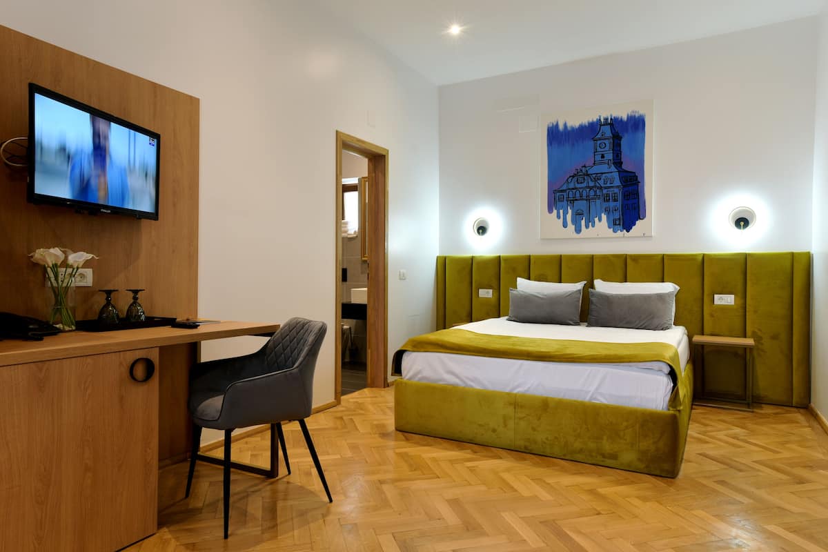 Une chambre moderne avec un bureau en bois, un lit doté d’une tête de lit verte et un tableau représentant un bâtiment accroché au mur.