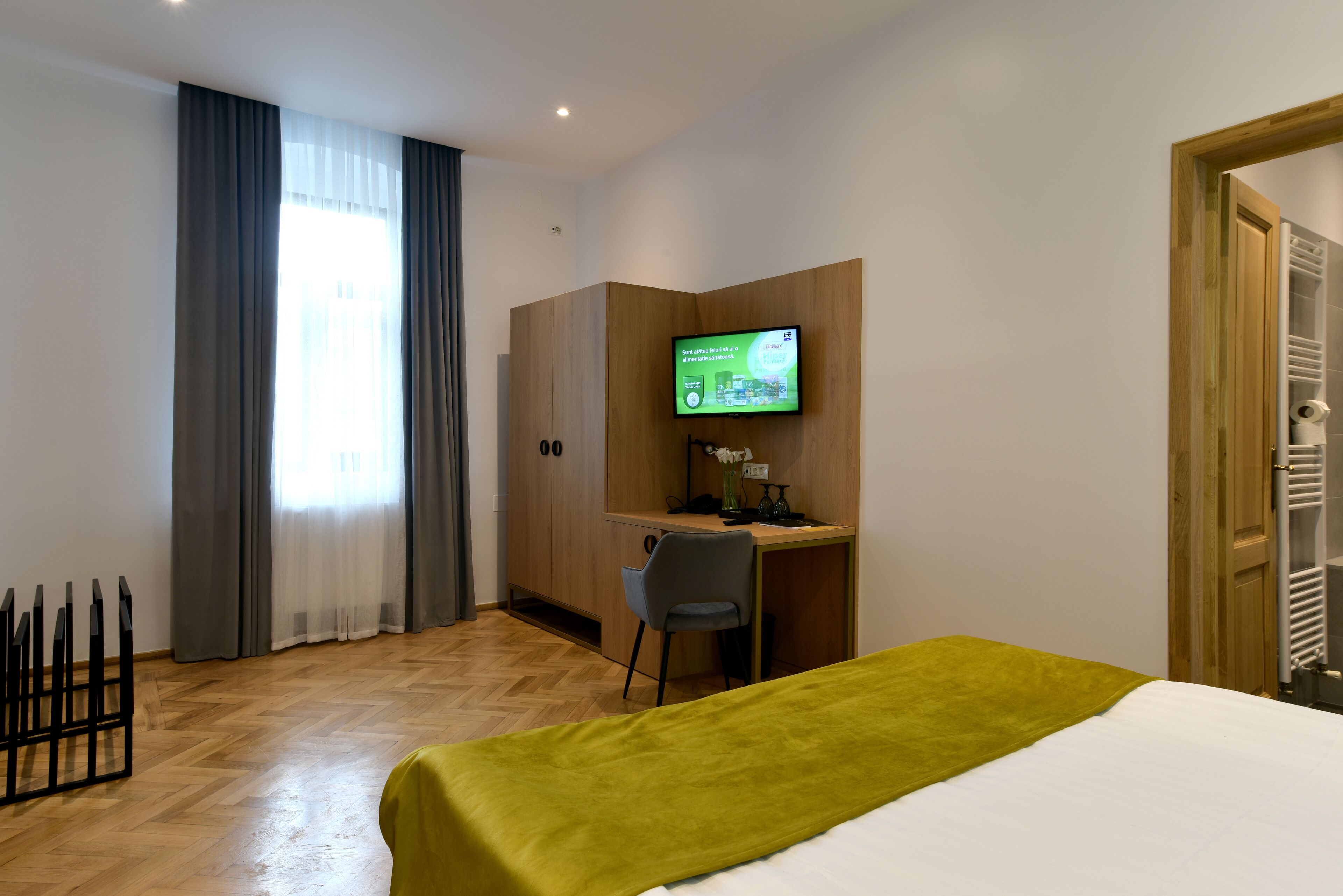 Habitación de hotel con cama, escritorio, silla, televisor y ventana con cortinas.