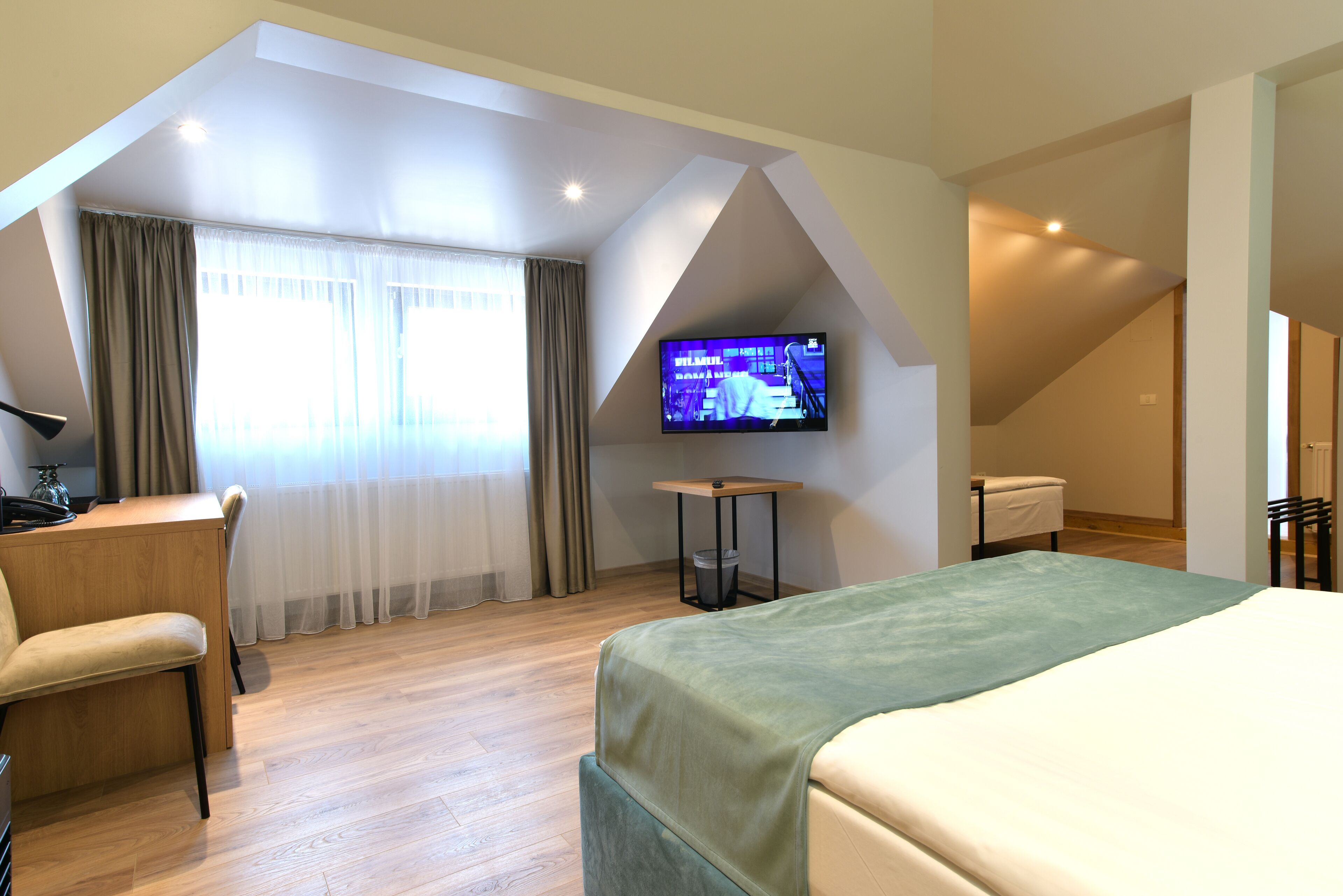 Una habitación de hotel con cama, escritorio, silla, televisor y ventana con cortinas.